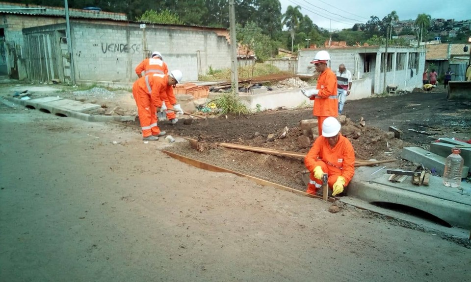 4 funcionários finalizando a construção de galeria, um abaixado,á direita; os demais em pé, com enxadas. Todos de uniforme laranja.